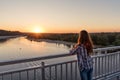 On a pier with steel railing over water stands girl young woman with her back with curly hair at sunset Royalty Free Stock Photo