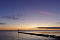 Pier before sunrise with small crane silhouetted against the morning sky and red vapor trail overhead Royalty Free Stock Photo