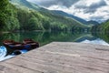 Pier with wooden row boats on the Biogradskoe lake. Sky with sun and clouds reflection. Bjelasica mountains, Kolasin, Biogradska Royalty Free Stock Photo