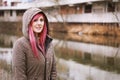 pierced young woman with pink hair and hooded parka standing by river