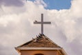 Pigeons roosting on a roof and on a cross against a dramatic cloudy sky