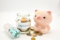 A piggy bank with a bandage at head with a pill container and an glasss bottle filled with coins on white background Royalty Free Stock Photo