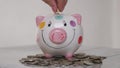 Piggy bank business standing on a pile of coins concept. A hand is putting a coin in a lifestyle piggy bank on a yellow Royalty Free Stock Photo