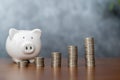 Piggy bank with coins on old wooden table. stack of coins and white smiling piggy bank for growth and saving with money box Saving Royalty Free Stock Photo