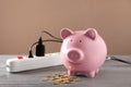 Piggy bank, coins and power strip on table. Electricity saving concept Royalty Free Stock Photo