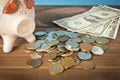 Piggy Bank and a few coins and dollar bills on the wooden table. Close up. The concept of saving money. Selective focus Royalty Free Stock Photo