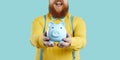 Piggy bank in form of blue pig in hands of joyful contented unrecognizable bearded fat man.