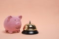 Piggy bank and gilded bell hotel service on pastel beige background.Conceptual, expensive hotel, travel and recreation