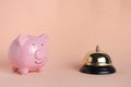 Piggy bank and gilded bell hotel service on pastel beige background.Conceptual, expensive hotel, travel and recreation