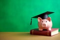 Piggy bank in graduation hat on book on green background. Cost of education in college and university Royalty Free Stock Photo