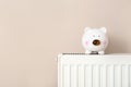 Piggy bank on heating radiator against light background. Royalty Free Stock Photo