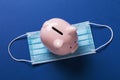 Piggy bank and medical mask on a blue background, top view Royalty Free Stock Photo