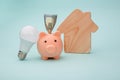 Piggy bank with money banknote and led light bulb, house figure on blue background. Energy saving concept Royalty Free Stock Photo