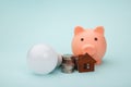 Piggy bank with money banknote and led light bulb, house figure on blue background. Power saving concept Royalty Free Stock Photo