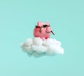 Piggy bank with pilot glasses flying on white fluffy cloud on turquoise blue background Royalty Free Stock Photo