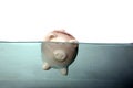 A piggy bank sinks in dark murkey water, representing the idea of drowning in debt, or keeping your head above water and other