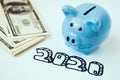 Piggy bank and stack of hundred dollar bills on background with marker inscription 2020 Royalty Free Stock Photo