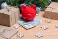 A piggy bank standing on cash dollars on a table with gift boxes, snowflakes and Christmas fir branches.