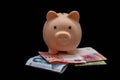 A piggy bank, standing on Chinese banknotes, with a 10 yuan bill inside on a black background. The concept of saving money. Royalty Free Stock Photo