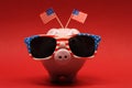 Piggy bank with sunglasses with USA flag and two small USA flags on red background