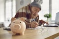 Piggy bank on table against background of frozen senior man paying utility bills online. Royalty Free Stock Photo