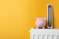 Piggy bank and thermometer on heating radiator against orange background, space for text Royalty Free Stock Photo