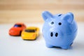 Piggy bank and two toy cars on white and wooden background