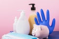 Piggy bank and various personal protective equipment on a pink background. Hygiene spending concept during coronavirus pandemic