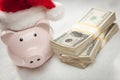 Piggy Bank Wearing Santa Hat Near Stacks of Hundred Dollar Bills on Snowflakes Royalty Free Stock Photo