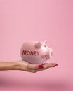 Piggy bank in a woman hand with inscription MONEY on a pink background. Minimal saving money concept