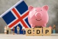 Piggy bank, wooden cubes with text, toy men made of plastic and the flag of Iceland on an abstract background