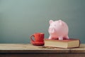 Piggy bank on wooden table with coffee cup and book. Saving money, budget planning