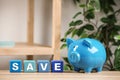 Piggy bank and word SAVE made of colorful cubes on wooden table against background