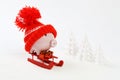 Piggy box with red hat with pompom standing on red sled and holding three gifts with gold bow on snow and around are snowbound Royalty Free Stock Photo