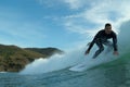 A young male surfer in a black wetsuit rides a white surfboard on a wave at Piha Beach, New Zealand