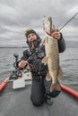 Pike fishing. Happy fisherman with big fish trophy at the boat with tackles Royalty Free Stock Photo