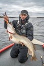 Pike fishing. Happy fisherman with big fish trophy at the boat with tackles Royalty Free Stock Photo