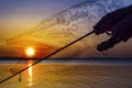 Pike fishing. Photo collage of silhouette of angler hands with spinning rod on soft focus muskie fish on sunset background Royalty Free Stock Photo