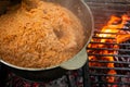 Pilaf cooking on fire outdoor. Open air kitchen at party picnic. Big pot with dish of rice and meat stays on wire rack and steams