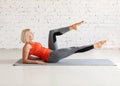 Pilates, abs workout. Attractive fit caucasian woman does practice sitting on a mat, in loft white studio indoor Royalty Free Stock Photo