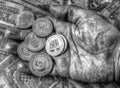 A pile of anniversary coins in a human`s hand over a background of banknotes in black and white