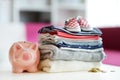 A pile of baby clothes, little shoes and a piggy bank. Parenting expenses concept. Working out a baby budget. Saving money when