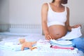 Pile of baby clothes, stuff and pregnant woman in home interior Royalty Free Stock Photo