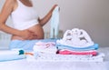 Pile of baby clothes, stuff and pregnant woman in home interior Royalty Free Stock Photo