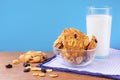 Pile of baked cruncy biscuits with cereal and raisins and glass of milk on blue towel. Concept