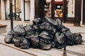 Pile of black garbage on the footpath at side road in big city, pollution trash. Many garbage plastic bags black waste