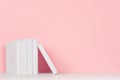 Pile blank white books on white desk and pastel pink background.