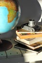 Pile of books, old film photo camera and a globe on white wooden table. Concept of travel, planning a dream trip