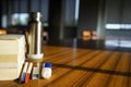 A pile of books, two different color pens, an iron water bottle, a correction fluid and note papers are placed on a wooden table.