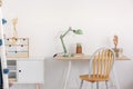 Pile of books, wooden hand and industrial mint colored lamp on stylish wooden desk in white kid`s bedroom